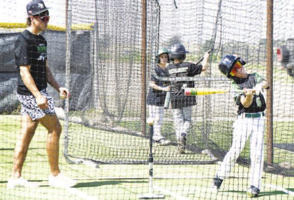 BATTING CAGES- A young camper takes a swing in the batting cages as a Ropes high school player offers instruction during the camp. (Staff photo by Trinity Boudreaux)