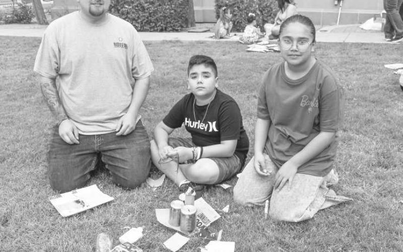 FAMILY FUN- The Kelly Hancock with the Chamber of Commerce taught children how to turn trash into art on Wendesday at the Library Summer Program on the Hockley County Courthouse lawn. Pictured is father Michael and Micaela Gonzalez and Mason Grant. (Staff photo by Emily Campos)