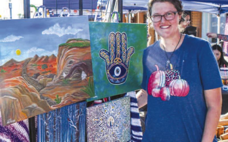 PAINTINGS – Jessica Allred smiled next to her paintings set up at the front of her booth during Saturday’s Falling for the Wallace festival in downtown Levelland. Other booths sold art alongside her on Houston Street. (Staff photo by Evin Thomas)