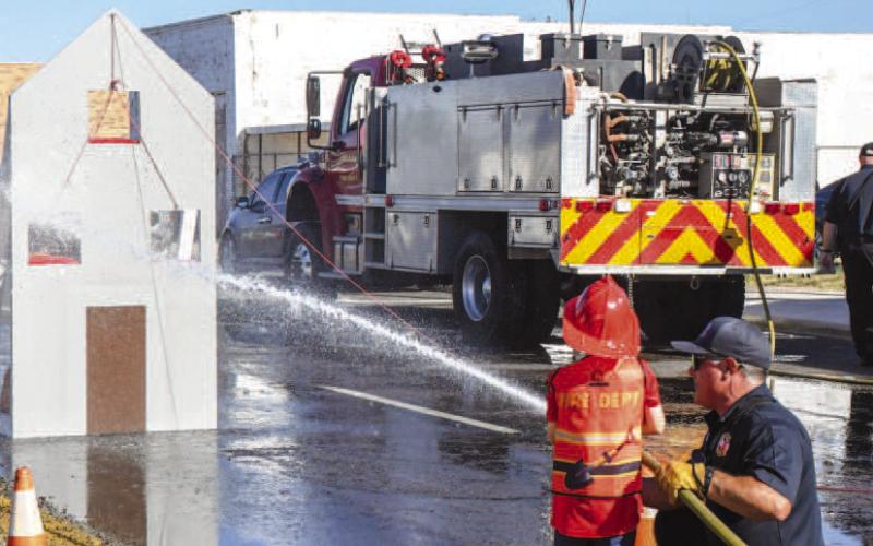 FIRE PREVENTION DAY – A child got help with holding a fire hose and spraying down a fake flaming house at downtown Levelland’s Falling for the Wallace festival on Saturday. The activity was a part of Levelland Fire Department’s (LFD) Fire Prevention Day, at which eventgoers could see fire equipment and speak with LFD personnel. (Staff photo by Evin Thomas)