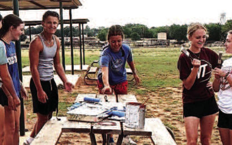 PAINTING TABLES - Sundown XC coaches Dakotah Watson and April Berry and team members joined in to paint city picnic tables as a community project. (Sundown ISD photo)