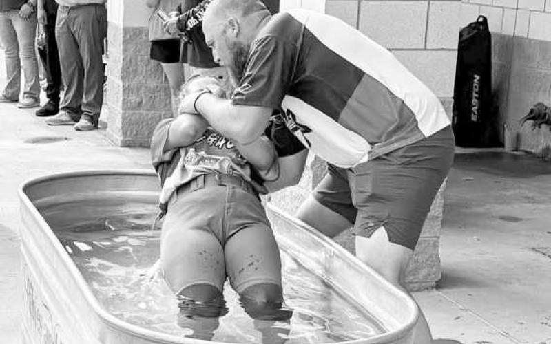 TROUGH BAPTISM – Flatland Fastpitch President Jacob Tucker baptizes one of his fully uniformed softball girls in a horse trough on June 29 at the OXY complex. (Staff photo by Jentezen Smith)