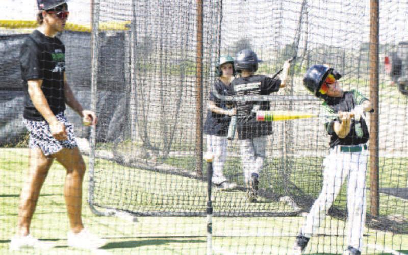 BATTING CAGES- A young camper takes a swing in the batting cages as a Ropes high school player offers instruction during the camp. (Staff photo by Trinity Boudreaux)
