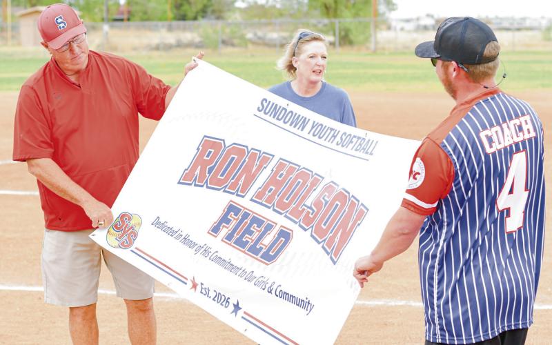BANNER UNVEILED - Sundown’s Ron Holson looks upon the unveiled banner to find the surprise of his name on it this past Thursday at Ron Holson Field in Sundown. Pictured with him is Youth League Manager Chad Harrell and his wife Crystal Holson. (Staff photo by Jentezen Smith)