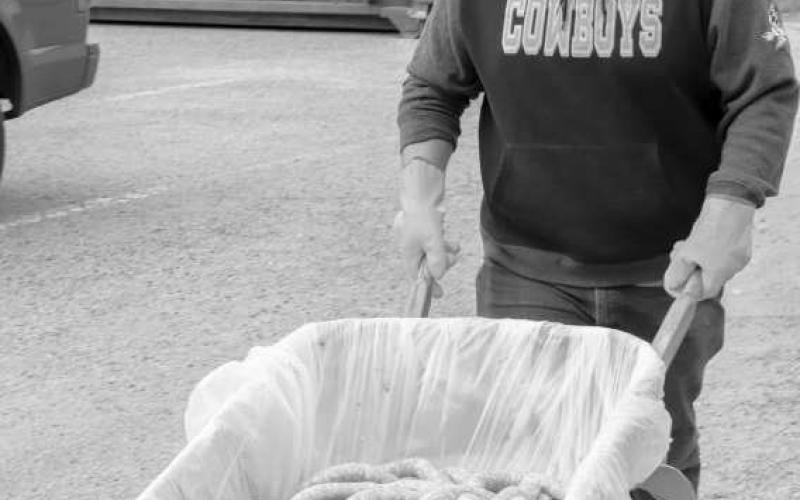 MOVING THE GOODS - Pictured is John Rodriguez wheeling the packed sausage to the smokehouse for cooking at St. Michael’s Catholic Church. (Staff photo by Adriana Solis)