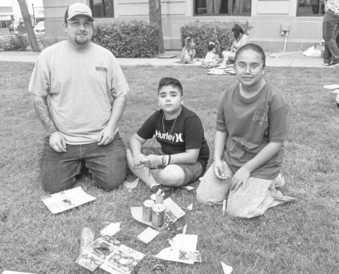 FAMILY FUN- The Kelly Hancock with the Chamber of Commerce taught children how to turn trash into art on Wendesday at the Library Summer Program on the Hockley County Courthouse lawn. Pictured is father Michael and Micaela Gonzalez and Mason Grant. (Staff photo by Emily Campos)