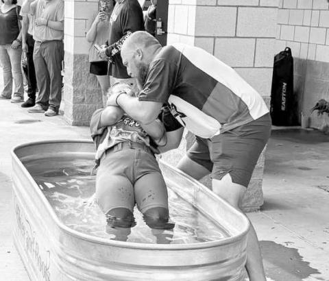 TROUGH BAPTISM – Flatland Fastpitch President Jacob Tucker baptizes one of his fully uniformed softball girls in a horse trough on June 29 at the OXY complex. (Staff photo by Jentezen Smith)